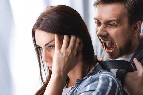 Depressed woman standing near angry screaming husband with waist belt on blurred background — Stock Photo