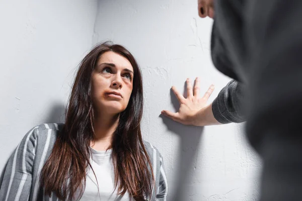 Woman with bruises on face looking at abuser on blurred foreground near walls — Stock Photo