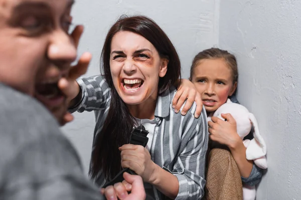 Angry woman with bruises on face slapping abusive husband near scared daughter — Stock Photo