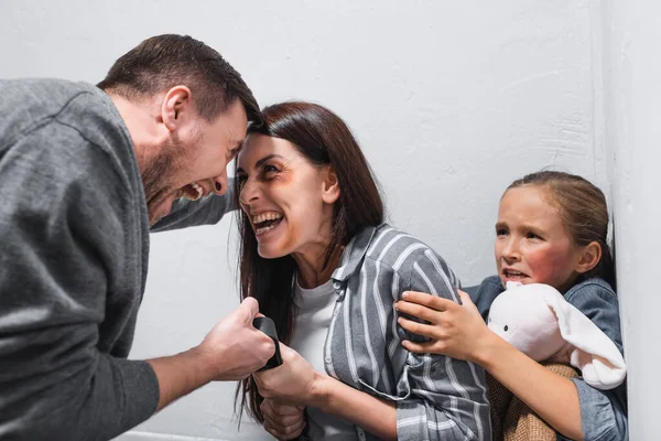 Femme hurlante avec des ecchymoses prenant ceinture des mains du mari près de pleurer fille — Stock Photo