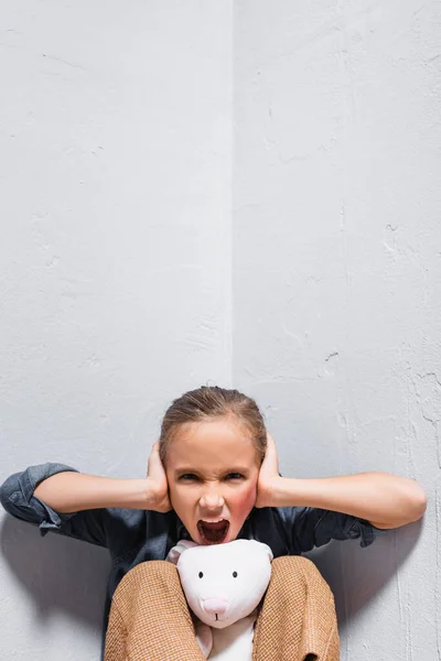 Victim of domestic abuse with soft toy screaming and covering ears — Stock Photo