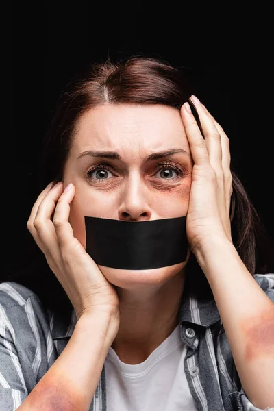 Portrait of woman with bruises and adhesive tape on mouth isolated on black — Stock Photo