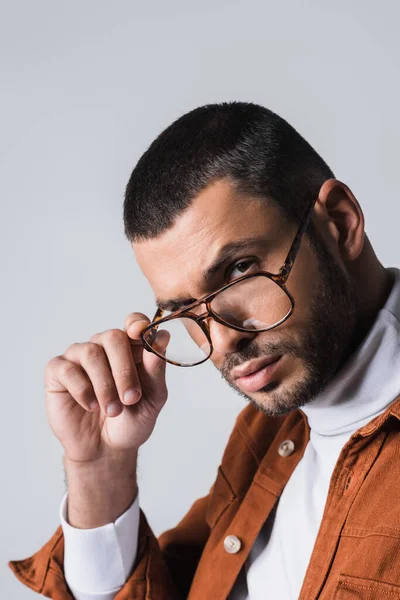 Elegante uomo barbuto che tiene gli occhiali e guarda la fotocamera isolata su grigio — Foto stock