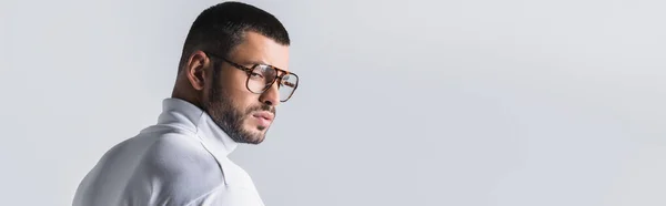 Hombre barbudo con gafas y cuello alto blanco mirando hacia otro lado aislado en gris, estandarte - foto de stock