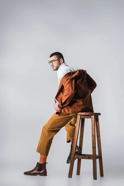 Модний чоловік у повсякденному одязі, сидячи на стільці на сірому фоні — стокове фото