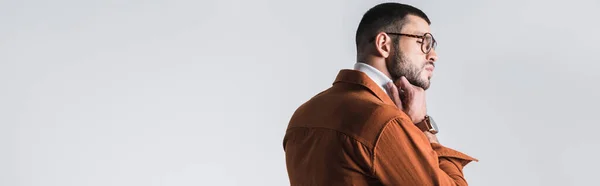 Elegante hombre con anteojos ajustando el cuello alto y mirando hacia otro lado aislado en gris, bandera - foto de stock