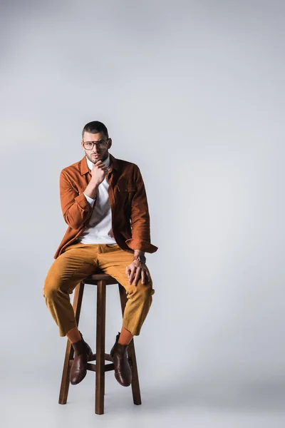 Hombre seguro y elegante sentado en una silla de madera sobre fondo gris - foto de stock