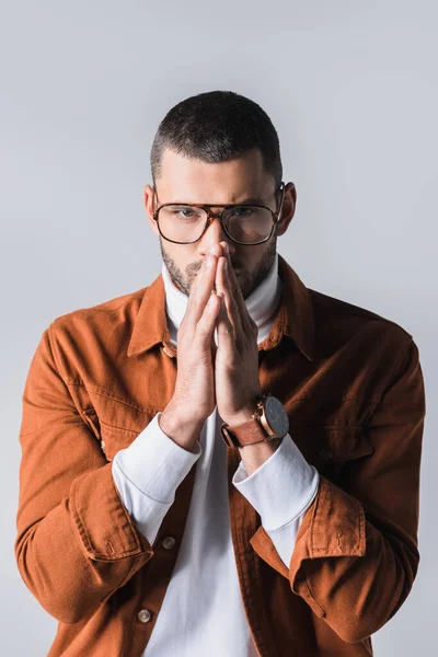 Стильний чоловік в окулярах з молитовними руками дивиться на камеру ізольовано на сірому — стокове фото