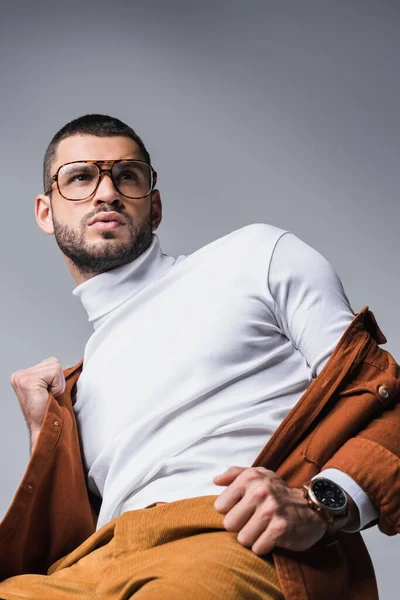 Vista de ángulo bajo del hombre barbudo sosteniendo chaqueta de terracota aislada en gris — Stock Photo