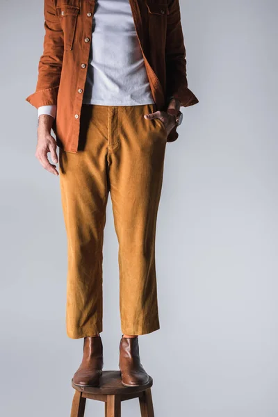 Cropped view of stylish man with hand in pocket standing on chair isolated on grey — Stock Photo