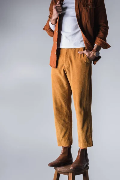 Cropped view of man in casual clothes and brown shoes standing on chair on grey background — Stock Photo