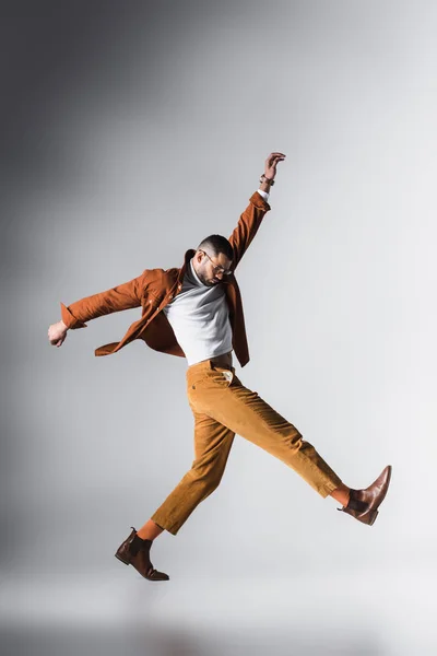 Jeune homme en lunettes, chaussures brunes et veste en terre cuite marchant sur fond gris — Photo de stock