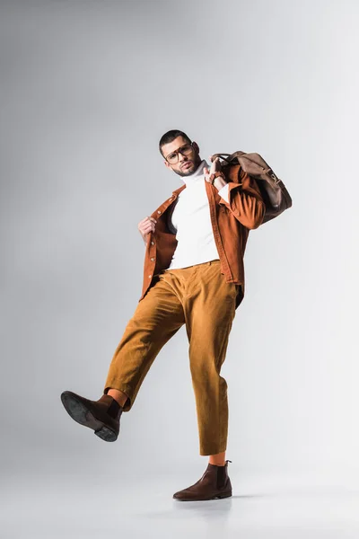 Vista de ángulo bajo del hombre de moda sosteniendo bolsa marrón y mirando a la cámara sobre fondo gris - foto de stock