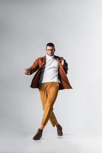 Hombre elegante mirando a la cámara mientras posa con el bolso sobre fondo gris - foto de stock