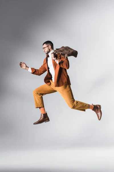 Elegante hombre barbudo con bolsa marrón en el aire sobre fondo gris - foto de stock