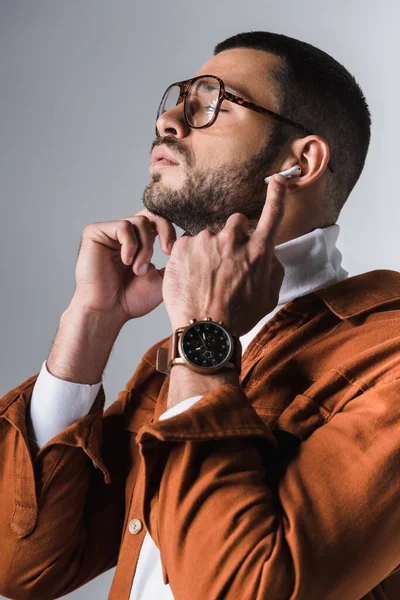 Стильний чоловік регулює навушники на сірому фоні — стокове фото