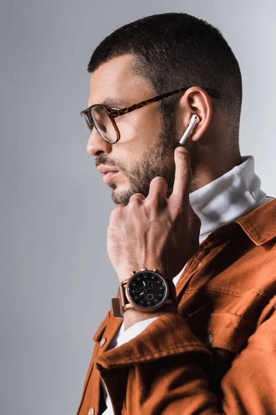 Бородатий чоловік вказує пальцем на бездротовий навушник на сірому фоні — стокове фото