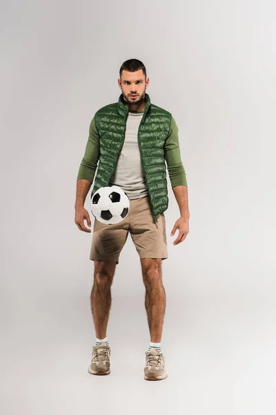 Bärtiger Mann blickt in die Kamera neben Fußball in der Luft auf grauem Hintergrund — Stockfoto