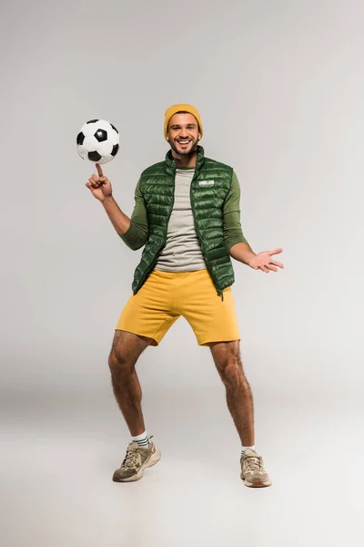 Sportsman sorridente alla macchina fotografica mentre tiene il calcio sul dito su sfondo grigio — Foto stock