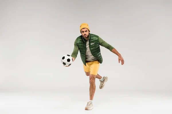 Young sportsman in casual clothes holding football while running on grey background — Stock Photo