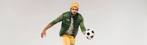 Bearded sportsman in hat holding football and looking at camera isolated on grey, banner — Stock Photo