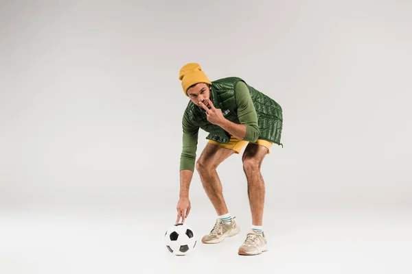 Esportista segurando futebol e apontando com os dedos para os olhos no fundo cinza — Fotografia de Stock