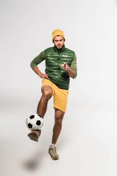 Serious sportsman pointing with finger at camera while playing football on white background — Stock Photo