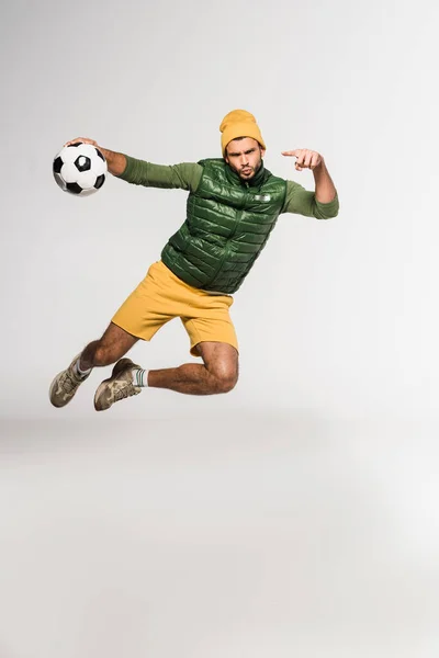 Sportsman apontando com o dedo para o futebol no ar em fundo cinza — Fotografia de Stock