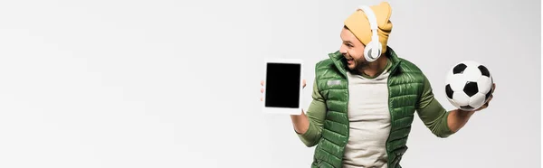 Homem alegre em fones de ouvido segurando tablet digital e futebol isolado em cinza, banner — Fotografia de Stock