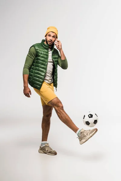 Sportif barbu parlant sur smartphone tout en jouant au football sur fond gris — Photo de stock