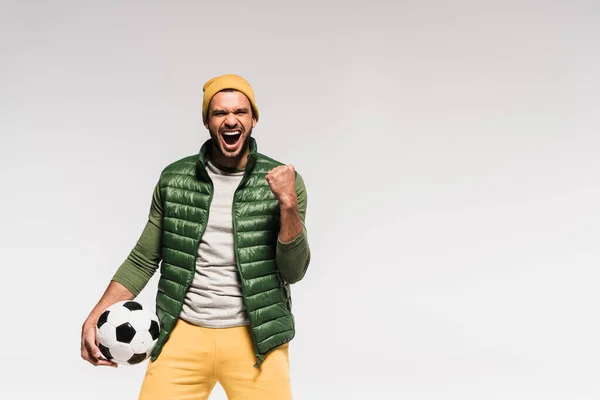 Excited sportsman in casual clothes showing yeah gesture and holding football isolated on grey — Stock Photo