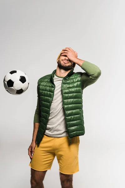 Sportsman covering face with hand near football in air isolated on grey — Stock Photo