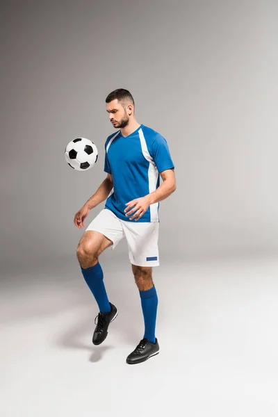 Bearded sportsman playing soccer on grey background — Stock Photo