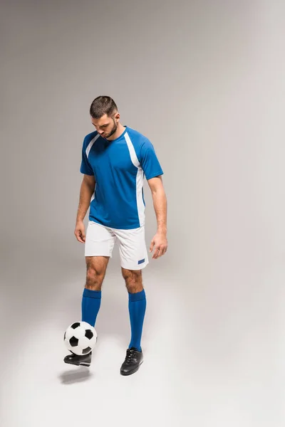 Jovem desportista em sportswear jogar futebol em fundo cinza — Fotografia de Stock