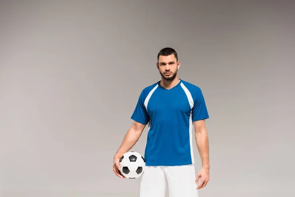 Deportista en ropa deportiva sosteniendo el fútbol y mirando a la cámara aislada en gris - foto de stock