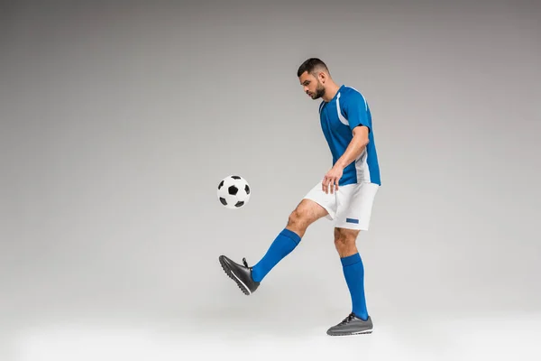 Man in sportswear playing soccer on grey background — Stock Photo