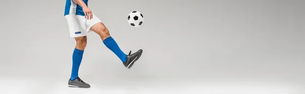 Обрезанный вид человека, играющего в футбол на сером фоне, баннер — стоковое фото
