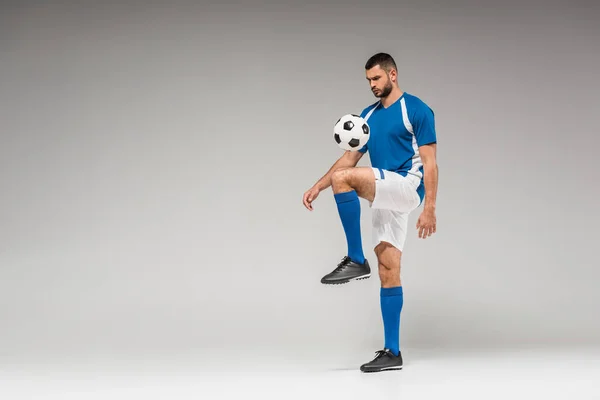 Bärtiger Sportler trainiert mit Fußball auf grauem Hintergrund — Stockfoto