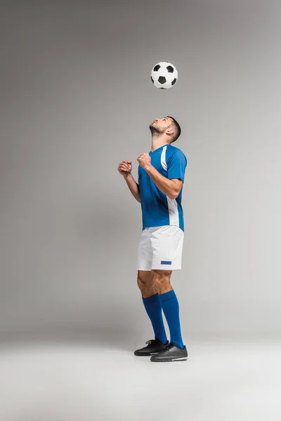 Jovem desportista olhando para o futebol no ar em fundo cinza — Fotografia de Stock