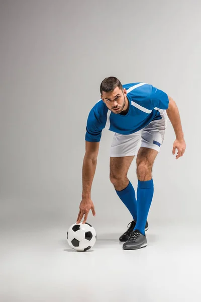 Selbstbewusster Sportler blickt vor grauem Hintergrund in die Fußballkamera — Stockfoto