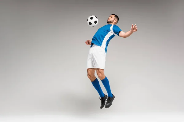Entrenamiento de deportista con fútbol mientras salta sobre fondo gris - foto de stock