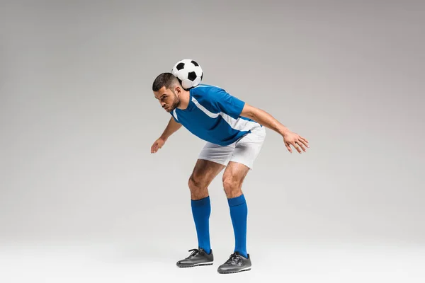 Спортсмен у спортивному одязі, що тримає футбол на сірому фоні — стокове фото