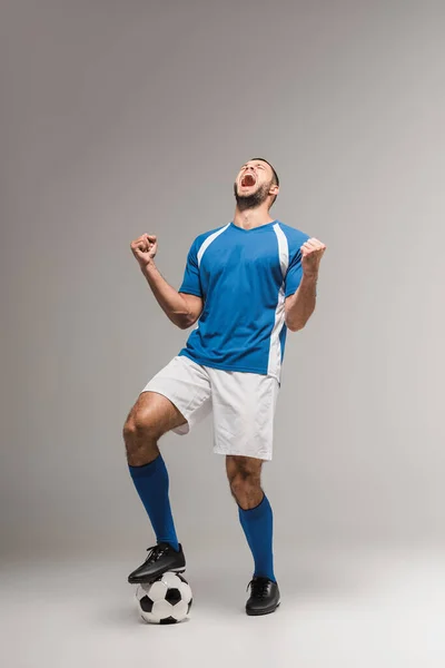 Deportista excitado en ropa deportiva mostrando sí gesto cerca del fútbol sobre fondo gris - foto de stock