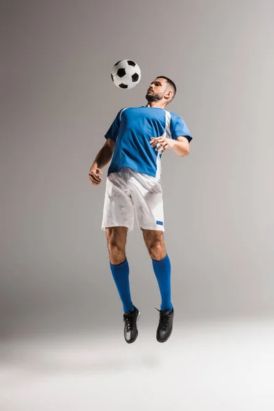 Спортсмен стрибає біля футболу під час тренувань на сірому фоні — стокове фото