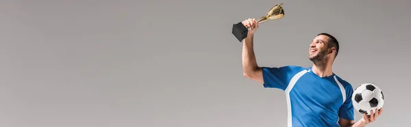 Sportsman sorrindo enquanto segurava copo dos campeões dourados e futebol isolado em cinza, banner — Fotografia de Stock