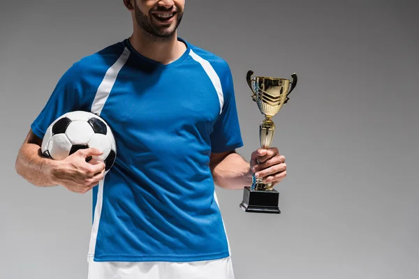 Vista ritagliata di sportivo sorridente con coppa campioni e calcio isolato su grigio — Foto stock