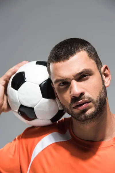 Retrato de desportista barbudo olhando para a câmera perto de futebol em fundo borrado isolado em cinza — Fotografia de Stock