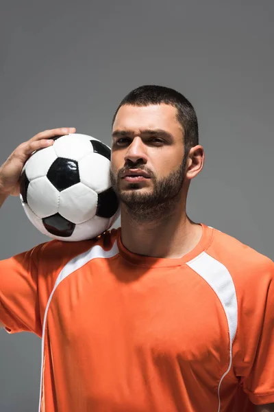 Deportista serio con fútbol mirando a la cámara mientras está de pie aislado en gris - foto de stock