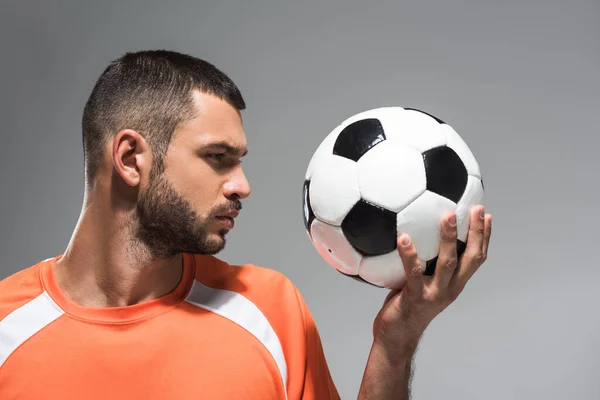 Молодий бородатий спортсмен дивиться на футбол ізольовано на сірому — стокове фото