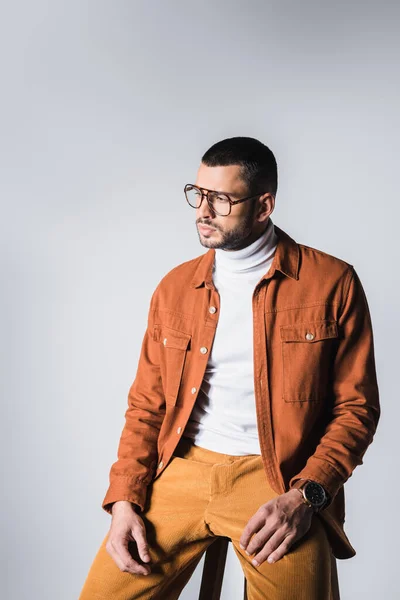 El hombre a la moda en las gafas de vista, sentado en la silla, aislado en gris - foto de stock